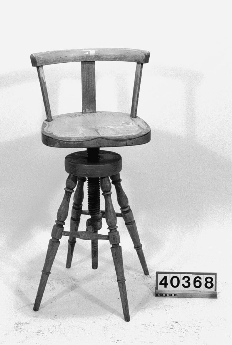 Kontorsstol, höjbar stol typ pulpet. Av trä. Fyrbent. Lägsta sitthöjd: 760 mm. Lågt ryggstöd: 280 mm, som är något trasigt. Otydlig text på sitsens undersida: Carl Fredrikssons träinrednings ... Katrineholm.