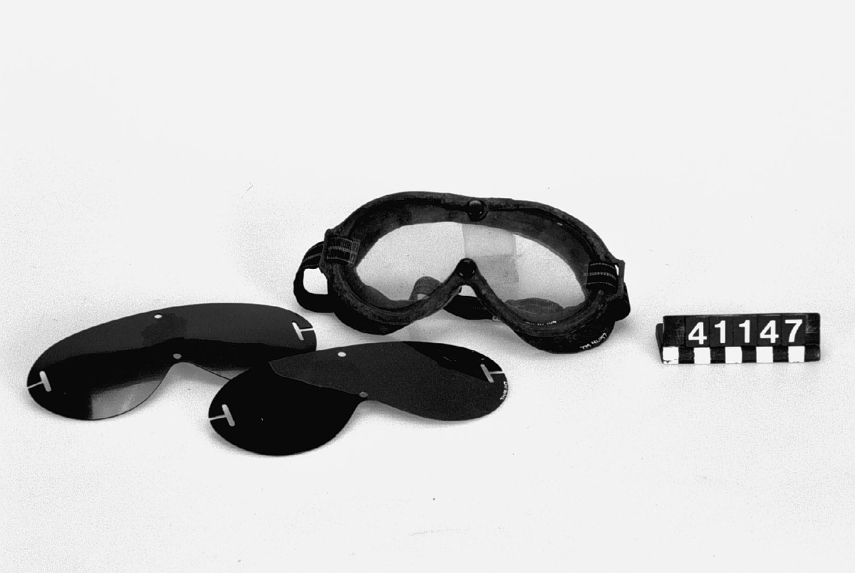 Motorcykelglasögon, i skyddsfodral av tyg.
Tillbehör: 2 lösa mörkfärgade glas.