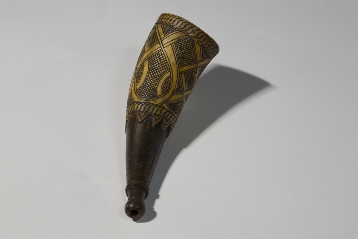 Krutthorn med bunnplate i tre med innskrift. Ornamentikk på horn i form av bånd i løkker mot en skravert bakgrunn. Punslet ornamentikk nærmere munningen.