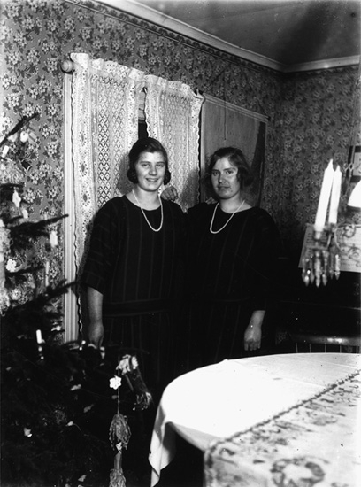 Rumsinteriör, två flickor vid julgranen.
Thea Elfrida och Linnéa Olsson, Erik Theon Olssons döttrar.