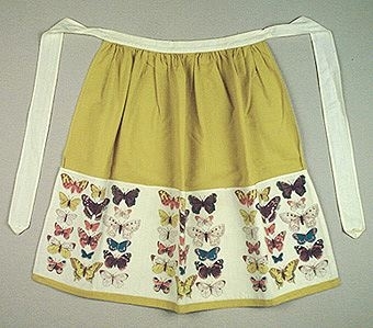 Midjeförkläde i grönt bomullstyg med ett påsytt tyg med tryckta, färgglada fjärilar på vit botten, indelat till tre fickor, Knytband 140 cm.