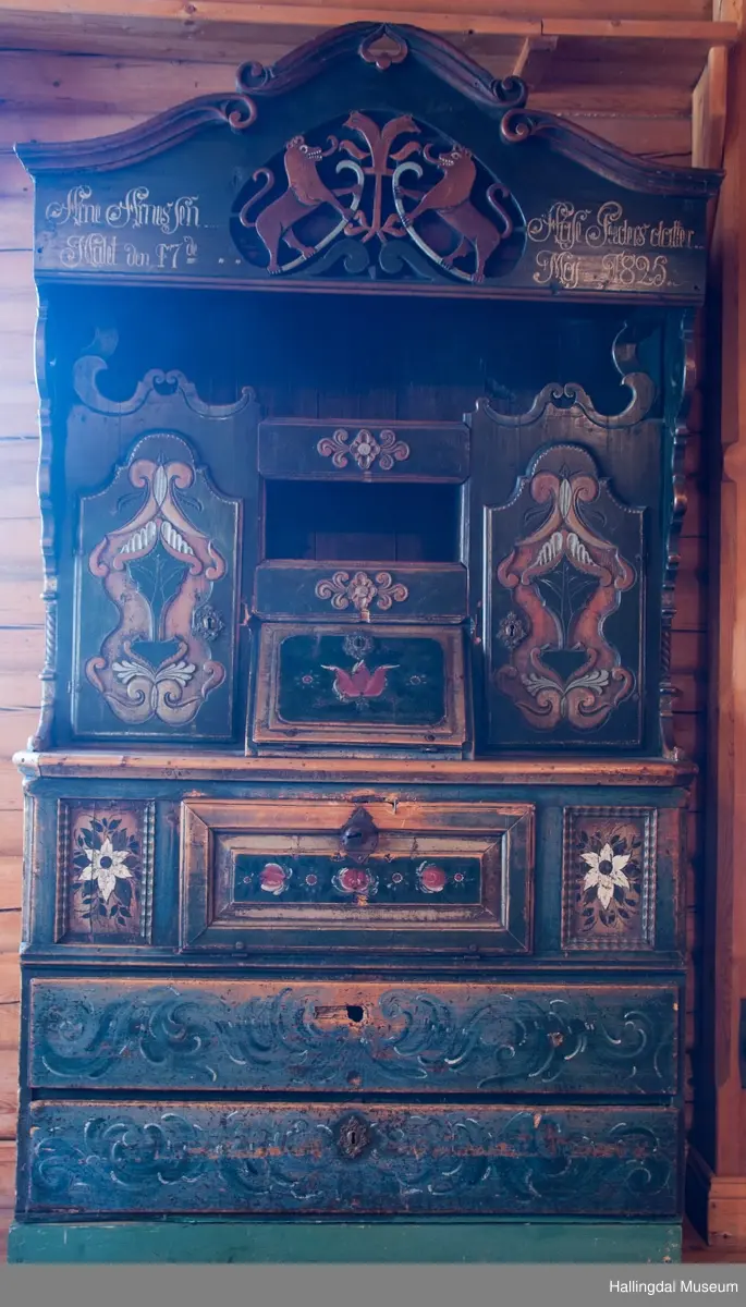 Delene satt sammen v.hj.a. tapping og trenagler.  Gavlen buede sider med skåret kronlist, delt i 3 profilerte, med opprullede ender.  Kronlister fortsetter på sidestykkene.  I toppen av kronlist hjerteformet, gj.brutt utskjæring opp ned.  Gavlens sentralfelt utskjæring i dyp flatskurd.  To løver, vendt mot hverandre, griper om hellebordskaft.  En stake som øverst kløyves i to bjørnehoder i profil skiller løvene.  Gavlen (el. baldakinens) forplate danner fremsiden i skuff i skapets bredde og dybde.  Overskapet:  Åpen hylle øverst, ca. 25 cm høy.  Under hyllen er det delt i 3 felt.  Ett skap i hvert sidefelt.  Midtfeltet har 2 skuffer adskilt av åpen hylle.  H. Skuffe: 12,5 cm.  H. åpent rom: 17 cm.  Under nederste skuff, skap med skråsider som stikker ca. 15 cm ut fra forveggen på overdelen.  Skapet dekkes av liggende skråklaff.  Festet jrenbeslag og hengsler nederst.  
En stor skuff i hele skapets bredde, 6 cm høy nederst, 32 cm dyp.  Over skuffen er rommet delt i 3 felt.  Hvert sidefelt har 2 skuffer og midfeltet en dyp skuff.  Midskuff har fylling med utskåret medaljong, klaff og hylle og skuffen rødmalt. .................................................