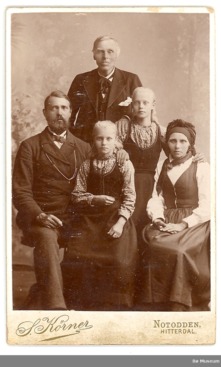 Familiegruppe på fem i fotoatelier.
På bildet sitter ekteparet Knut T. Haugestul og Gunhild Jørgensdtr. t.v. og h. Tvillingdøtrene Åste t.v. og Guro t.h.
Bror til Gunhild, Guttorm J. Firingen, står bak.