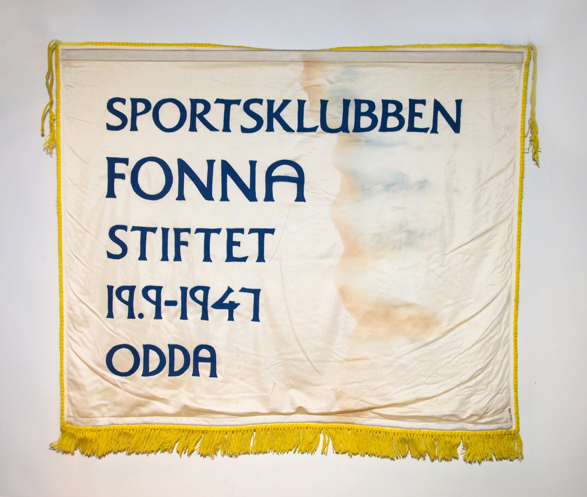 Motiv på ei side av fana er logo for sportsklubben Fonna: blå oval sirkel, gul inni, kvit vimpel med teksten FONNA på tvers av sirkel