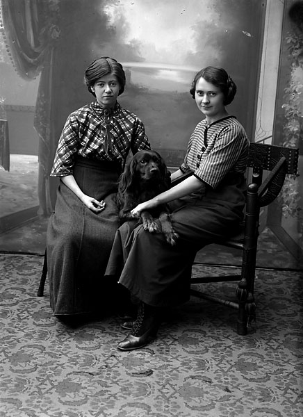 Ateljébild två kvinnor och en hund, ”1912 F” på asken
	Metallutfällning.