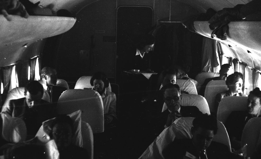 Luftfoto. Ombord i et fly, LN-HAT, DC-54A fra Braathens SAFE, slapper passasjerene av mens en flyvertinne serverer forfriskninger.