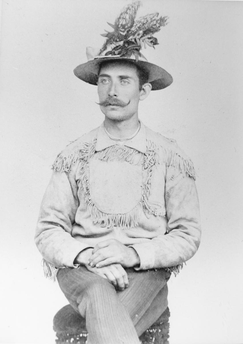 Selvportrett av Anders Andersson, med kjerringrokk og rogneblader i hatten, og jakke med frynser i "indianerstil".