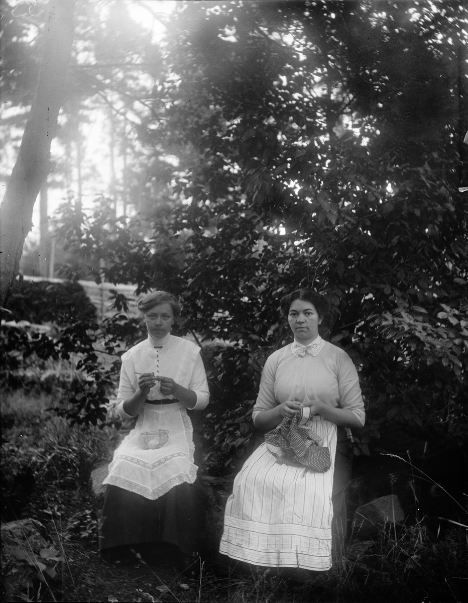 Två kvinnor handarbetar i trädgården, 1910-tal