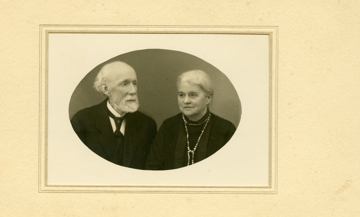 Portrett av en eldre kvinne og mann. Kvinnen er iført en mørk kjole med halssmykke mens mannen er iført dress og slips.