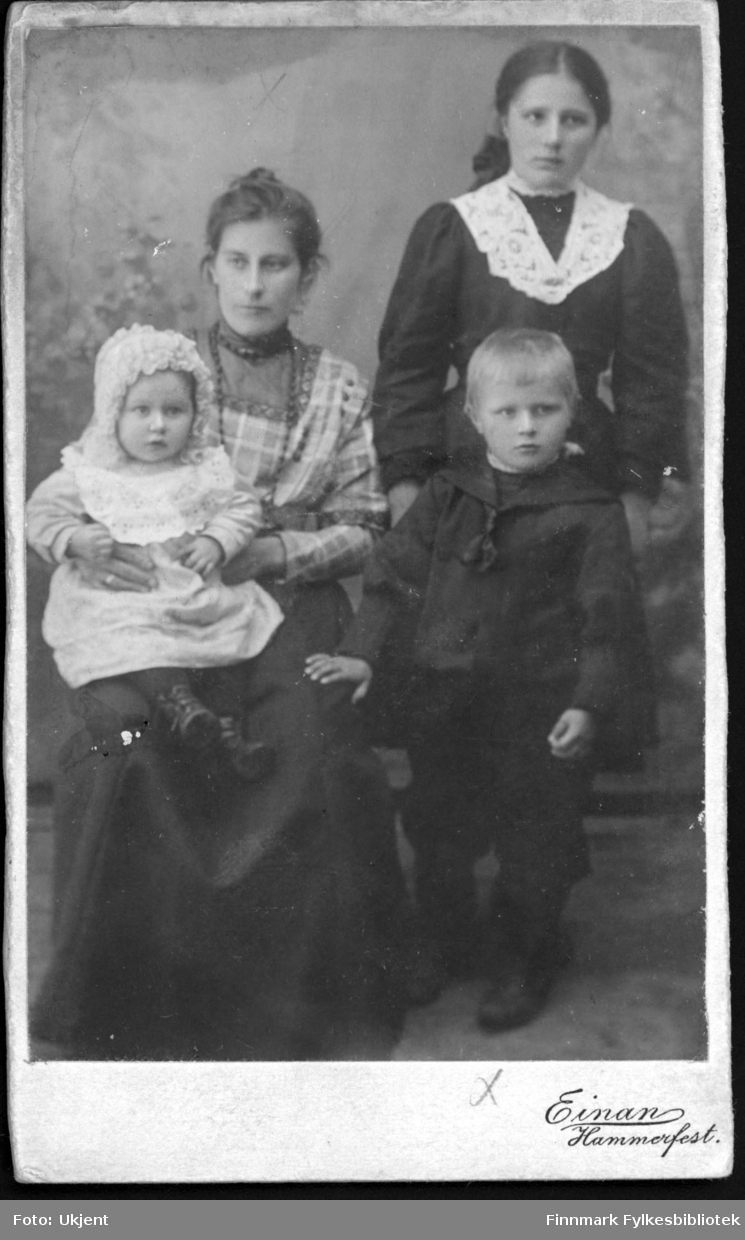 Et portrett av Amanda Mathisen med barna Magnhild (venstre) og Wilhelm (høyre). Amandas kusine Anna Dahl står bak den lille Wilhelm. Kvinnene har på seg kjoler, Amanda har et smykke rundt halsen. Magnhild har på seg en hette av noe slag og Wilhelm har en maritim - inspirert skjorte på seg.