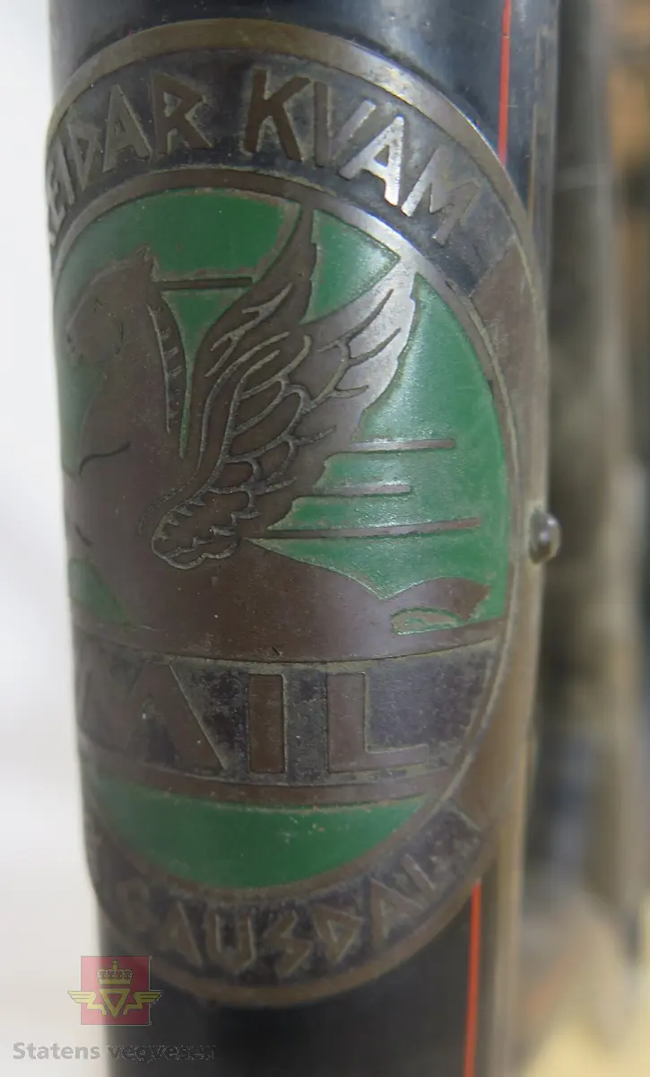 Tråsykkel, damemodell. Har to hjul, styre, sete, pedaler, frontlykt, ringeklokke, bagasjebrett, dynamo og refleks bak. Svart med rød staffering. Brunt sete og røde holker på styret. Sykkelen er i hovedsak lagd av metall, gummi og skinn.
Emblem med teksten: REIDAR KVAM Ø. GAUSDAL MIL.