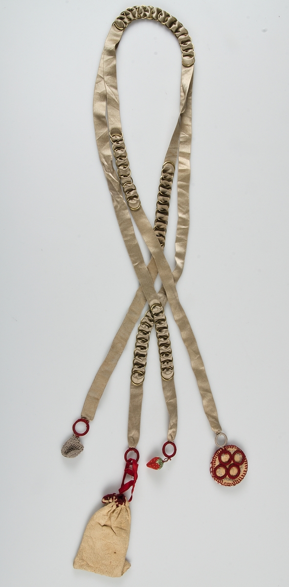 Beigefärgat silkeband, dubbelt, med sämskskinnspung, nålbok, smultron och liten virkad pung fäst i olika ändar.

