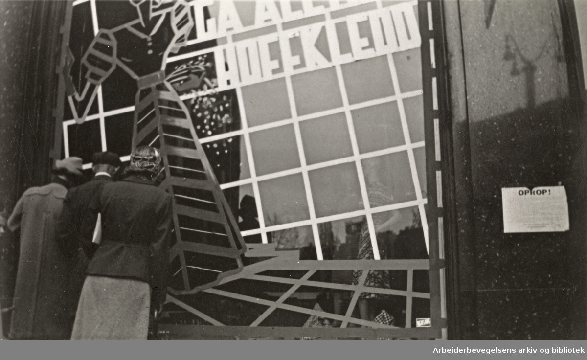 Ole M. Engelsens fotografier fra okkupasjonsårene i Oslo. Slik ble vindusrutene sikret for å hindre at glasset skulle splintres ved flyangrep. ."Gå alltid Hoffkledd"..Bildet er tatt utenfor Hoff damekonfeksjon i Karls Johans gate 25, mai 1940.