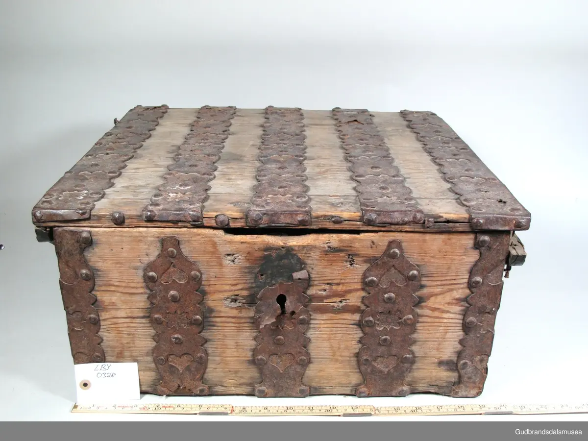 "Ferdaskrin. Umalt. Over heile skrinet går det beslag med innhogga stjerner og hjerter. Fra Østre Gausdal. Merknad 2, også kalla Føringsskrin" (Jf. Katalog for Lom Bygdesamling, 1925).
Skrinet har 1 rom. LOKK: satt sammen av 3 bord, holdt sammen av sidelister på innsiden og jernbeslag langs sidekanter på oversiden. Hengslet med 2 hengselbeslag på innsiden og  2 på utsiden av bakstykke.  1 stk. låsbeslag på innsiden av lokk.
SKRINSIDER: gjæra sammen, holdt sammen av hjørnekantbeslag utvendig; profilerte toppkanter.
BUNN: satt sammen av 2 bord, festet til skrinrammen med trenagler. Er i tillegg opprinnelig holdt på plass av 10 beslag festet til skrinbunn og sidestykker. Jernhandtak på hver side.
BESLAG: 5 jernbeslag i lengderetning på lokk. Tilsvarende 3 beslag og 2 hjørnebeslag på front og sider. Alle beslag er festet med jernnagler.
DEKOR. Ingen skurd- eller malingdekor. Skrinet har i stedet jernbeslag med utskårne hjerte- og stjerneformer som dekor. Muligvis fra 1600-tallet der treskurden ikke var fremherskende. Liknende dekor ses på LBY0319.
BRUK. Før kofferten kom i bruk hadde man reiseskrinet, som ble brukt til oppbevaring av bl.a. klær, verdisaker og mat på reiser. Skrinet hadde ofte et eller to mindre, smale rom langs den ene skrinsiden og ett større rom. De fleste reiseskrin var i tillegg forsterket med jernbeslag langs alle kanter og med en solid nøkkelhullås til sikring mot støt, slag og tyveri.