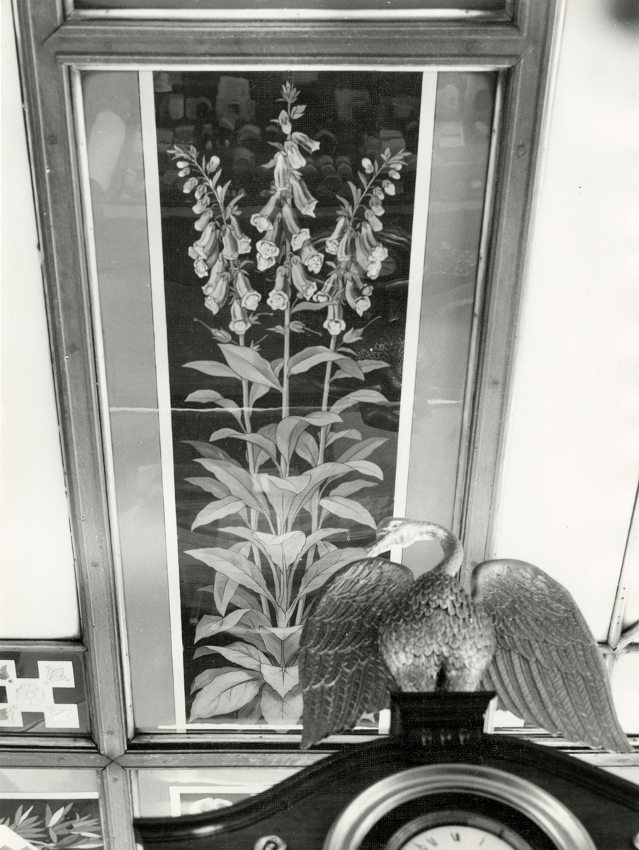 Fotografi av interiørdetalj med glassmaleri av revebjelle samt svanefigur.