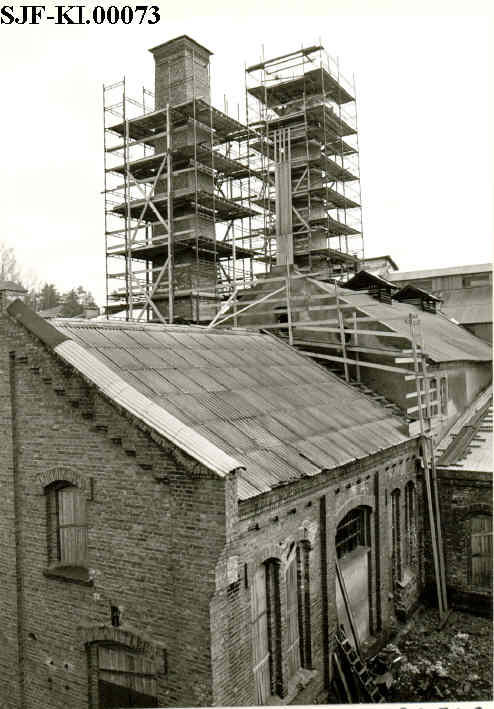 Fabrikken i forfall. Bildet viser restuareringsarbeidet på fabrikken. Stillaser er satt opp rundt to store piper og taket repareres.