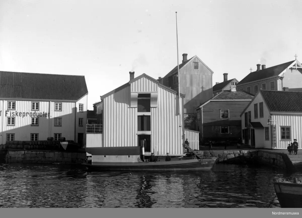 Et bilde av sundbåten Kvik til kai på Innlandet i Kristiansund. Tollbua og Dødeladen. Kjønnøybrygga. Nordmøre Museums fotosamling. dublett av FAKf-100296.186986
