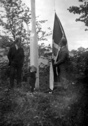 To menn og en liten gutt i ferd med å heise flagget. Dette e