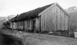 Foto av et eldre gårdshus med torvtak beliggende ved en land