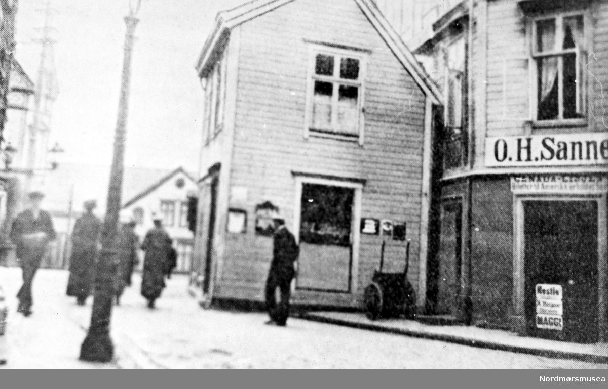 Foto fra Lindahls plass omkring 1890-1910, hvor vi ser "kommoden" - et hus som stod ute i gaten vis-a-vis Hvedings butikk/bygård. "Kommoden" ble senere revet omlag 1910. Det var Gullsmed Unhjem som var den siste som hadde forretning i denne gården, og vi ser skiltet i vinduet. Til høyre ser vi O. H. Sannes. Her kunne man få kjøpt biletter til Canada-linjen. Som skiltet sier: "CANADA-LINJEN Biletter til Amerika erholdes her". Samt reklame-plakater for Nestle,  A. Bergene Chocolade og Maggi buljong. Ellers så ser vi
I bakgrunnen Loennechengården. Fra Nordmøre museums fotosamlinger.