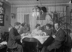 To menn og tre kvinner er samlet til måltid rundt spiseborde