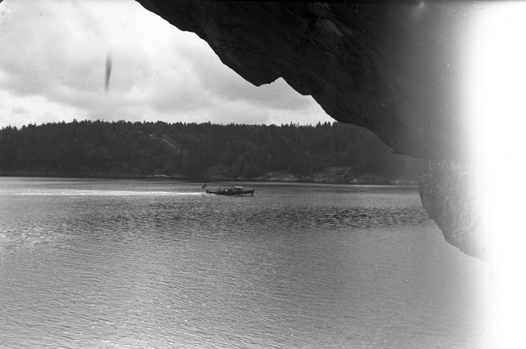 Utsikt över en sjö med klippa i förgrunden.
På bilden kör en båt förbi.
OBS! Lite ljusskadat till höger av bilden!