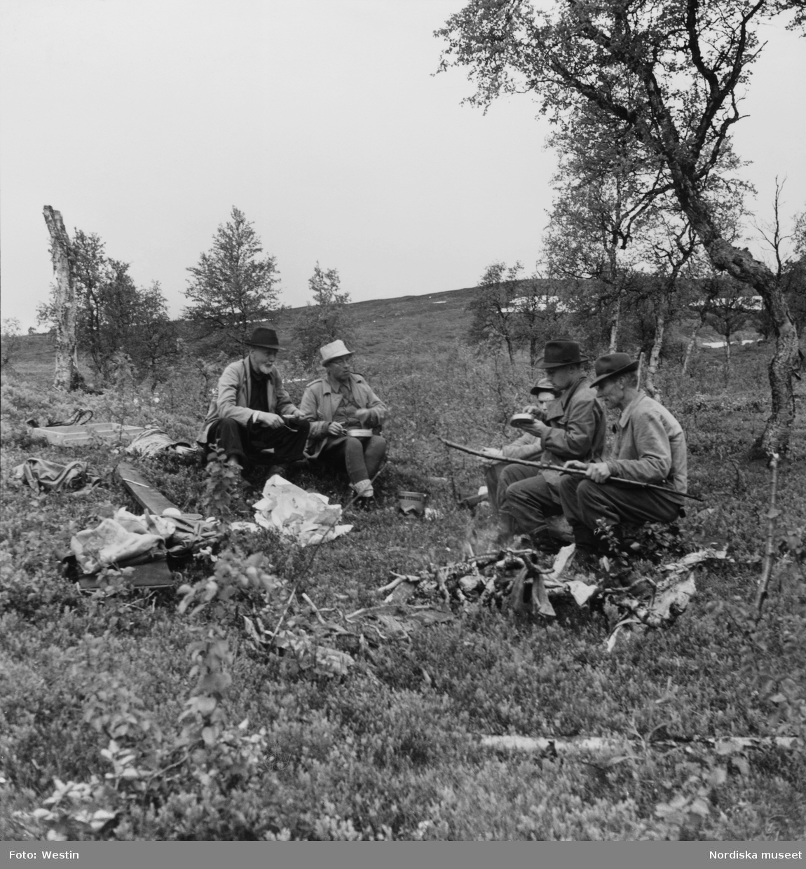 Från utgrävningen av "stalotomterna" vid Brantsfjället. Fem män vilar och äter matsäck. Under Nordiska museets Lappmarksundersökning.