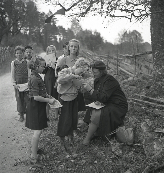 Orientering 1942. 
En lärarinna hjälper några elever, sittande vid en väg.