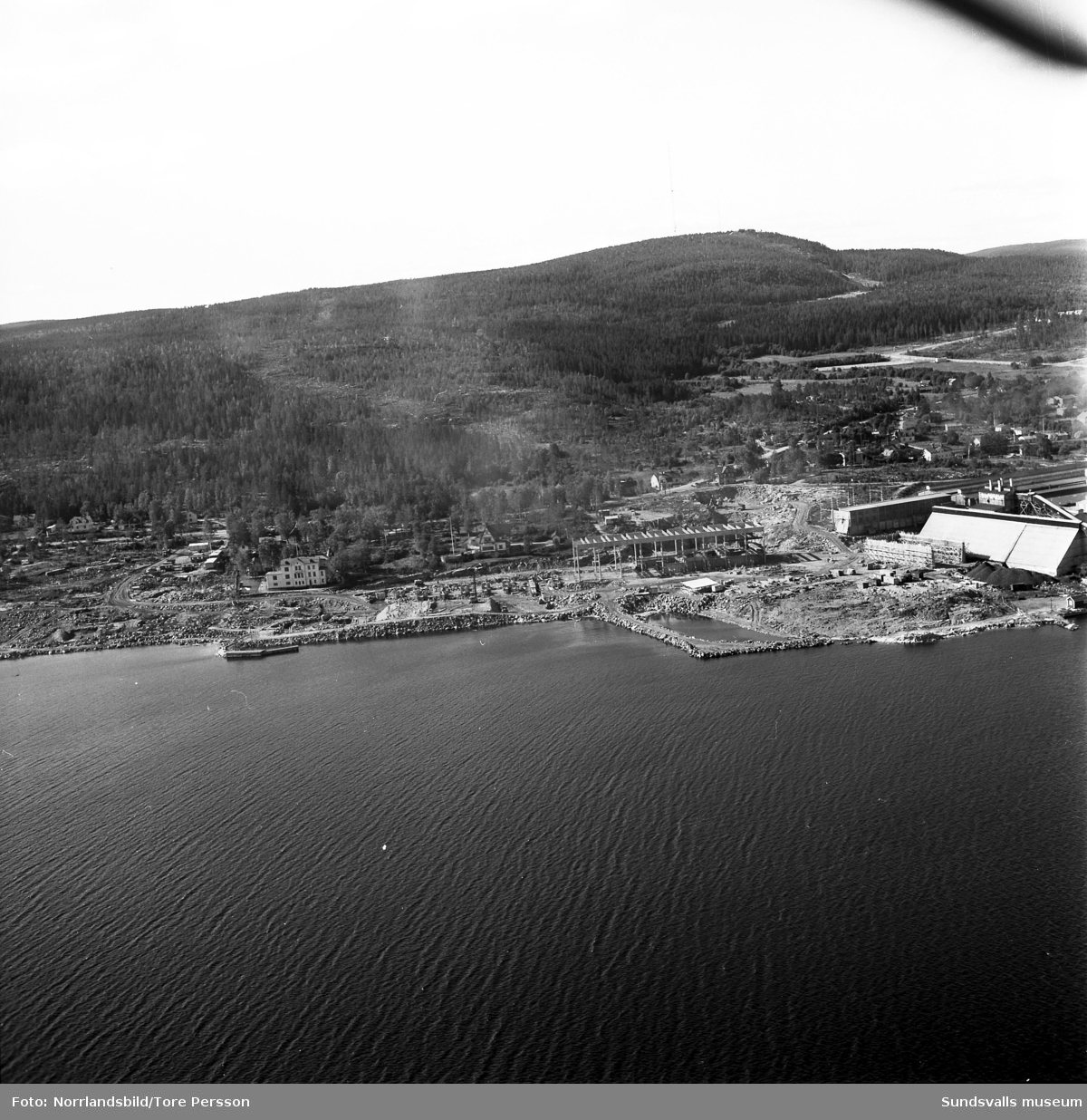 Flygfoton över Kumo där sommarparadisen Villa Kumo och Villa Steninge trängs undan av Aluminiumkompaniets (Aloxidverken, Gränges, Kubal) stora nybygge.