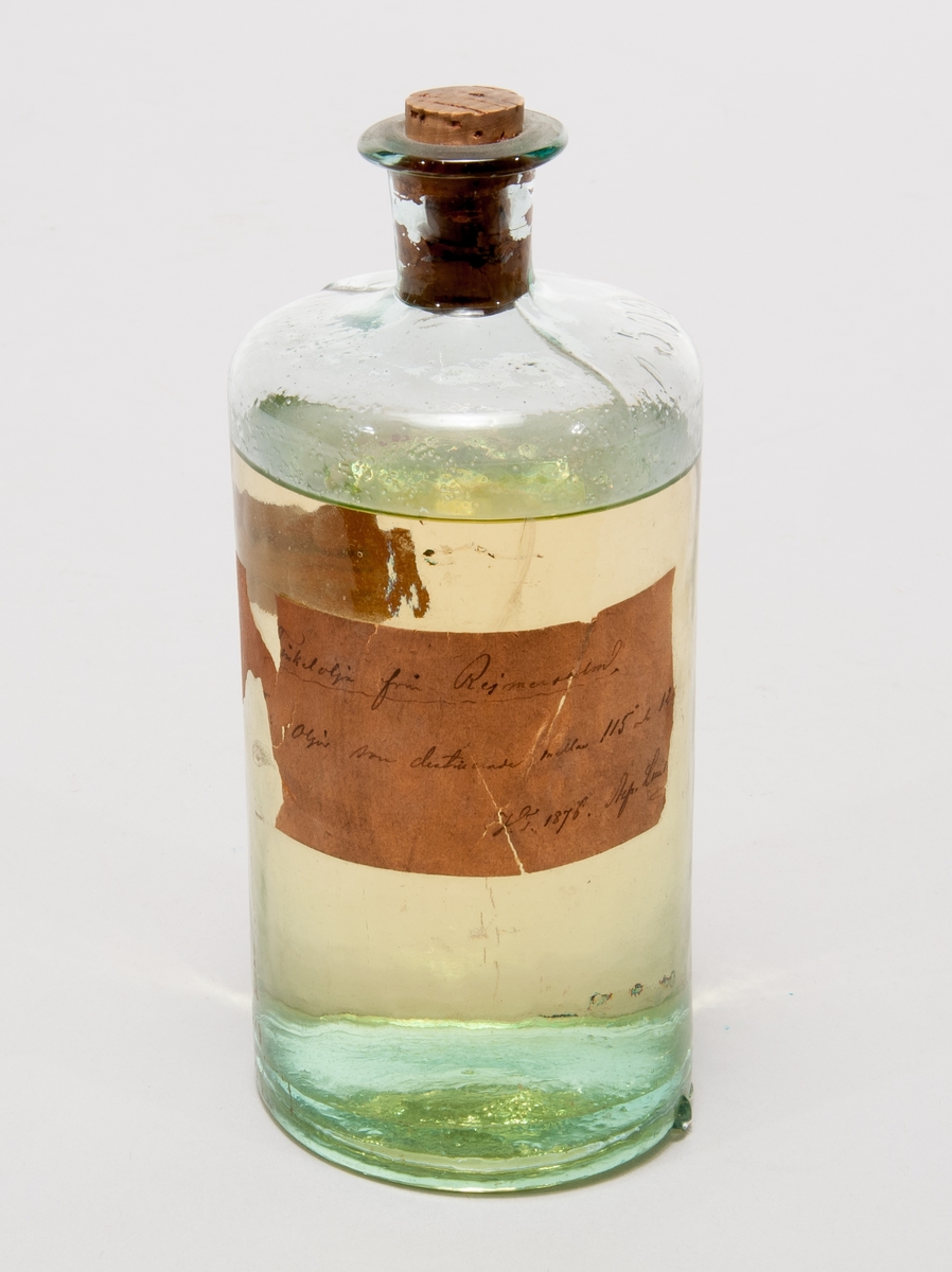 Finkelolja i  flaska av glas med etikett:  "Finkelolja från Reymersholm. II: olja, som destillerade mellan 115 grader celcius och 120 grader celcius. V.T. Alfr. Lundberg."