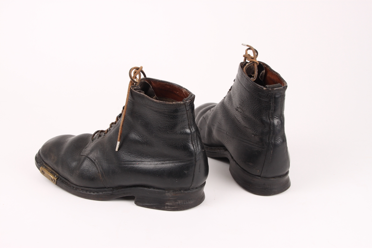 Skistøvler i lær med lærlisser. Skoene har seks hull under støvelen til bindingsfeste, samt metallbeslag foran på sidene av sålen.