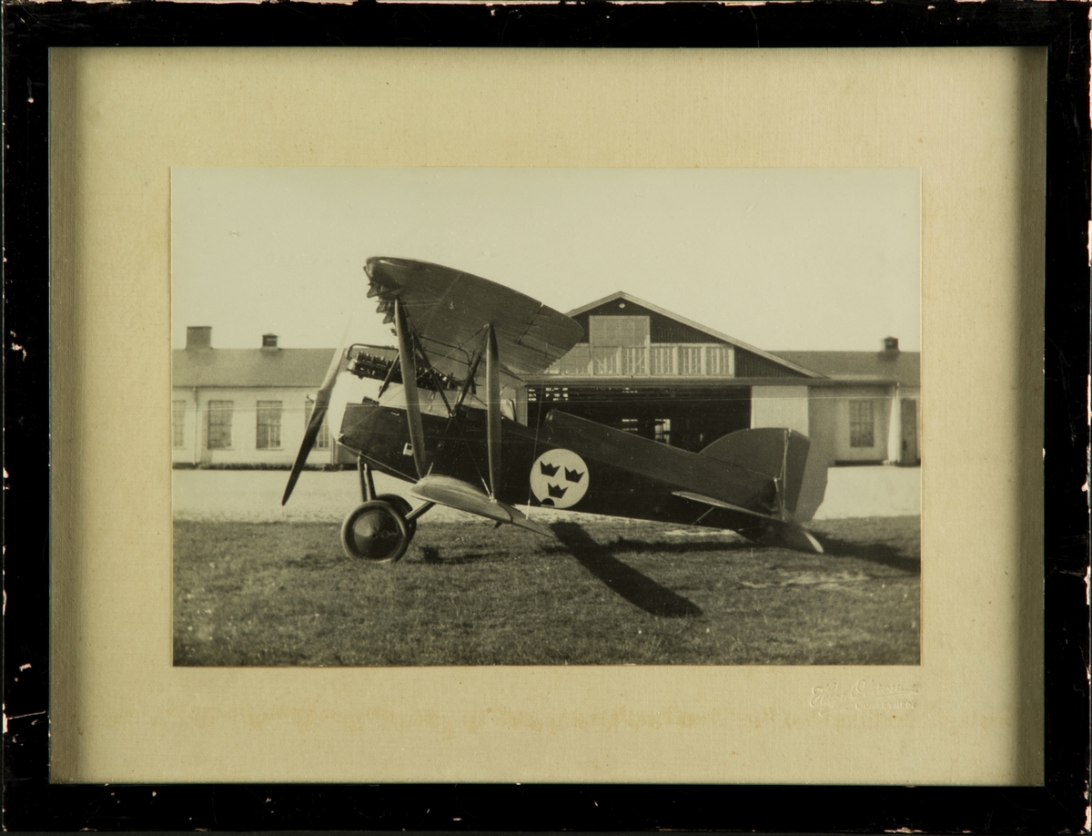 Jaktflygplan J 1 står framför en hangar på F 5 Krigsflygskolan. Inramat foto.