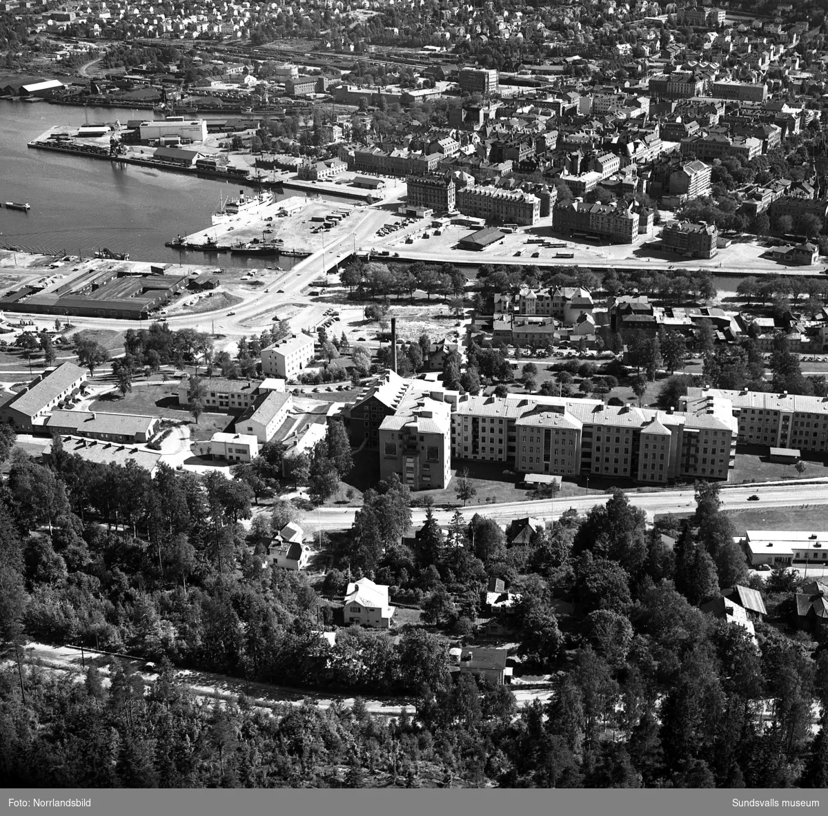 Flygfoto över Stenstaden och hamnen tagen söderut från Norra berget. Sjukhuset närmast, kvarteret Notvarpet på Norrmalm är rivet men ännu inte bebyggt och i bildens övre vänstra del syns gasklockan vid Landsvägsallén (kvarteret Rosenborg).