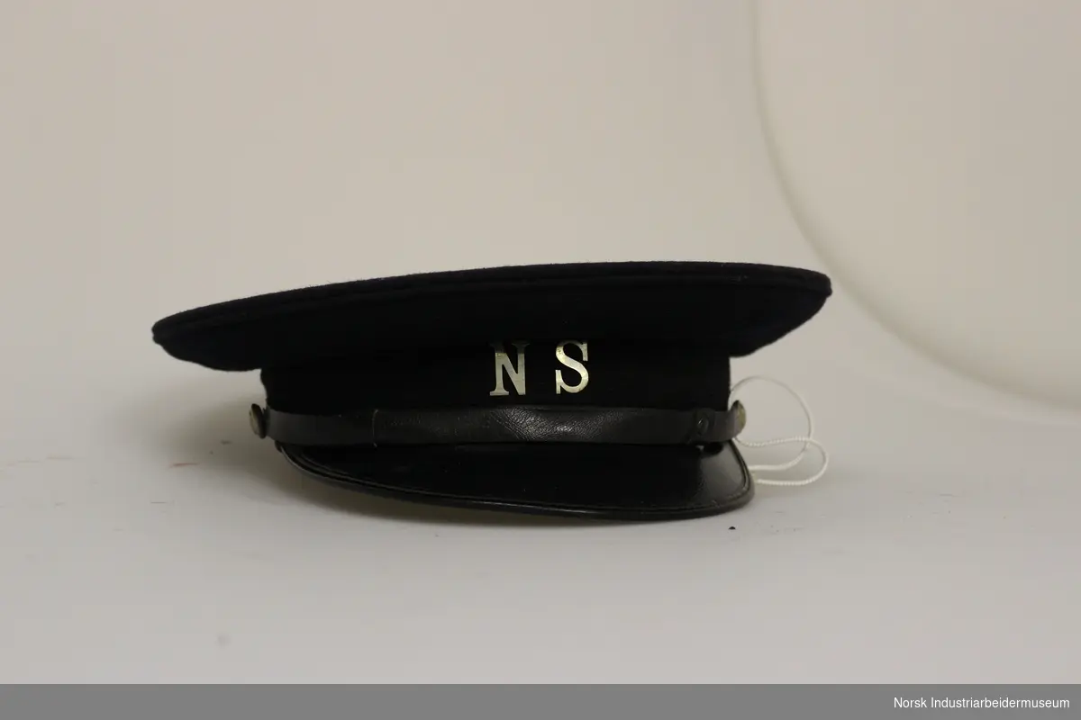 Blå uniformslue med sort skygge og N S i metall i front.
Str. 57