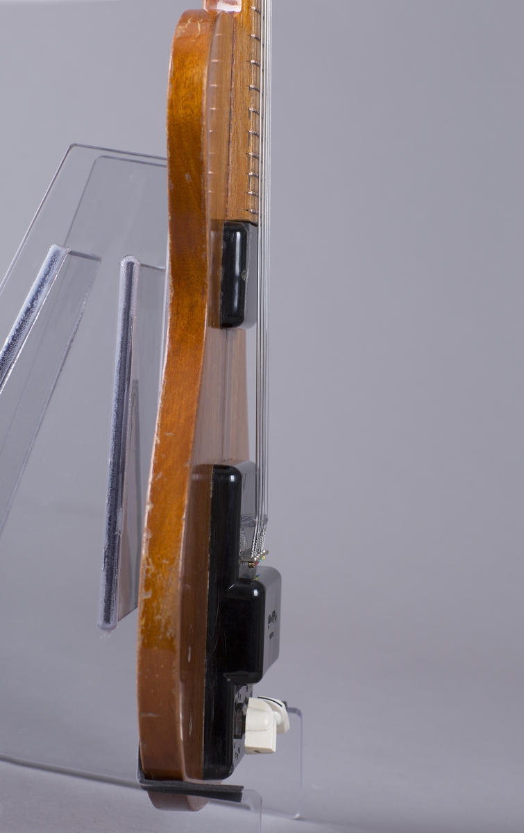 Elektrisk gitar med kropp og hals av mahogny. Magnet ved halsfeste og pickup ved strengefeste (NilsensSystem). Kontrollere for tilpasning og klangfarge. Tilpasning tilsvarer volum og gir størst volum på nivå 1. Enkelte av stemmeskruene er ikke originale.