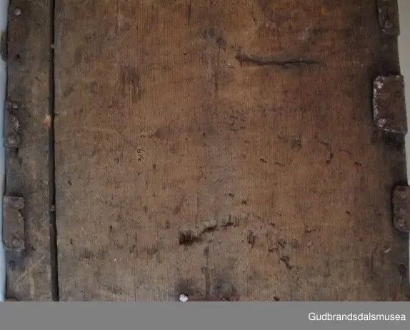 "Rik gjenombroten jarning over heile skrinet. Gamal type, alder uviss. Fra Vestre Gausdal". (Jf. "Katalog for Lom Bygdesamling,1925"). 
Skrinet har 3 rom, nøkkelhullslås og jernhandtak på sidene. Lokket er satt sammen av 2 bord, er festet til utsiden på bakstykket med to hengselbeslag og har 2 sidelister festet med trenagler. Bunnen er satt sammen av 2 bord, festet til hverandre med 2 forsenka trenagler; bunnen er festet til skrinrammen med trenagler.  Skrinrammen er tappet og forsterket med hjørnekantbeslag utvendig. 
Skrinet har jernbeslag med gjennombrutt mønster, 5 stk. B: 6,5 x L: 45 cm på lokk, 3 på hhv. bakstykke, front og sidestykker B: 6,5 x 20 cm. Lokket har ett låsbeslag og de to øvre hengselbeslag festet på innsiden, de to nedre hengselbeslag er festet på utsiden av bakstykket. Alle beslag er festet med store jernnagler samt festet under bunn på skrinet. De to hengselbeslag har også gjennombrutt mønster.  Nøkkelhullslåsen mangler låsanordning på innsiden.
DEKOR. Malingen har blitt beskyttet med et lag ferniss el.l., noe som ble vanlig fra begynnelsen av 1700-tallet. Ingen skurddekor. I stedet er beslag av jern brukt som dekorelement, noe som periodemessig kan peke på 1600-tallet, tidlig 1700-tallet, der treskurden ikke var fremherskende. Liknende dekorbruk finner du på LBY0328. Skrinet har gjennombrutt mønster på beslag og store jernnagler som beslagfeste. Treverket som synes mellom beslagene er malt med horisontale bølgestrukturer i gul og brun. Den dominerende dekorfargen er brun og gul, men det finnes små rester av blå eller blågrønn på lokk, sidelister på lokk, front og bunnkant på bakstykket samt av gul på frontbeslag. Innsiden av lokket er malt i terracottarød nyanse. Tradisjonelt fremkom denne fargen ved bruk av saft fra orr blandet med spytt, som ble smurt ut over treet. 
BRUK. Før kofferten kom i bruk hadde man reiseskrinet, som ble brukt til oppbevaring av bl.a. klær, verdisaker og mat på reiser. Skrinet hadde ofte et eller to mindre, smale rom langs den ene skrinsiden og ett større rom. De fleste reiseskrin var i tillegg forsterket med jernbeslag langs alle kanter og med en solid nøkkelhullås til sikring mot støt, slag og tyveri.