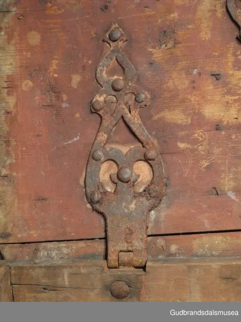 "Rik gjenombroten jarning over heile skrinet. Gamal type, alder uviss. Fra Vestre Gausdal". (Jf. "Katalog for Lom Bygdesamling,1925"). 
Skrinet har 3 rom, nøkkelhullslås og jernhandtak på sidene. Lokket er satt sammen av 2 bord, er festet til utsiden på bakstykket med to hengselbeslag og har 2 sidelister festet med trenagler. Bunnen er satt sammen av 2 bord, festet til hverandre med 2 forsenka trenagler; bunnen er festet til skrinrammen med trenagler.  Skrinrammen er tappet og forsterket med hjørnekantbeslag utvendig. 
Skrinet har jernbeslag med gjennombrutt mønster, 5 stk. B: 6,5 x L: 45 cm på lokk, 3 på hhv. bakstykke, front og sidestykker B: 6,5 x 20 cm. Lokket har ett låsbeslag og de to øvre hengselbeslag festet på innsiden, de to nedre hengselbeslag er festet på utsiden av bakstykket. Alle beslag er festet med store jernnagler samt festet under bunn på skrinet. De to hengselbeslag har også gjennombrutt mønster.  Nøkkelhullslåsen mangler låsanordning på innsiden.
DEKOR. Malingen har blitt beskyttet med et lag ferniss el.l., noe som ble vanlig fra begynnelsen av 1700-tallet. Ingen skurddekor. I stedet er beslag av jern brukt som dekorelement, noe som periodemessig kan peke på 1600-tallet, tidlig 1700-tallet, der treskurden ikke var fremherskende. Liknende dekorbruk finner du på LBY0328. Skrinet har gjennombrutt mønster på beslag og store jernnagler som beslagfeste. Treverket som synes mellom beslagene er malt med horisontale bølgestrukturer i gul og brun. Den dominerende dekorfargen er brun og gul, men det finnes små rester av blå eller blågrønn på lokk, sidelister på lokk, front og bunnkant på bakstykket samt av gul på frontbeslag. Innsiden av lokket er malt i terracottarød nyanse. Tradisjonelt fremkom denne fargen ved bruk av saft fra orr blandet med spytt, som ble smurt ut over treet. 
BRUK. Før kofferten kom i bruk hadde man reiseskrinet, som ble brukt til oppbevaring av bl.a. klær, verdisaker og mat på reiser. Skrinet hadde ofte et eller to mindre, smale rom langs den ene skrinsiden og ett større rom. De fleste reiseskrin var i tillegg forsterket med jernbeslag langs alle kanter og med en solid nøkkelhullås til sikring mot støt, slag og tyveri.