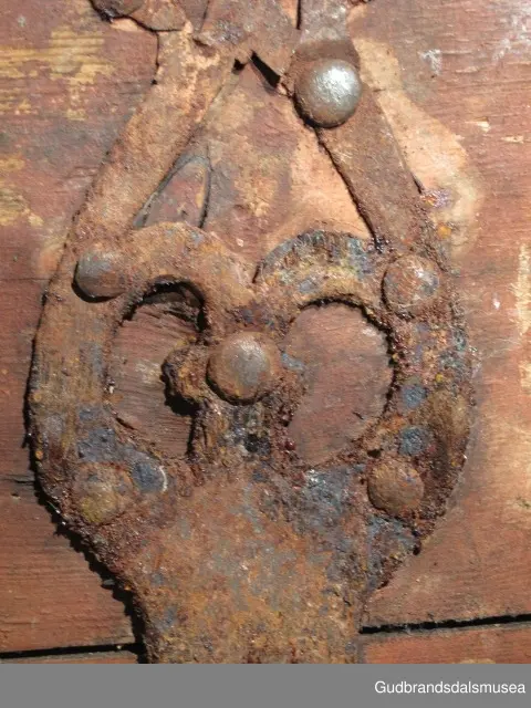 "Rik gjenombroten jarning over heile skrinet. Gamal type, alder uviss. Fra Vestre Gausdal". (Jf. "Katalog for Lom Bygdesamling,1925"). 
Skrinet har 3 rom, nøkkelhullslås og jernhandtak på sidene. Lokket er satt sammen av 2 bord, er festet til utsiden på bakstykket med to hengselbeslag og har 2 sidelister festet med trenagler. Bunnen er satt sammen av 2 bord, festet til hverandre med 2 forsenka trenagler; bunnen er festet til skrinrammen med trenagler.  Skrinrammen er tappet og forsterket med hjørnekantbeslag utvendig. 
Skrinet har jernbeslag med gjennombrutt mønster, 5 stk. B: 6,5 x L: 45 cm på lokk, 3 på hhv. bakstykke, front og sidestykker B: 6,5 x 20 cm. Lokket har ett låsbeslag og de to øvre hengselbeslag festet på innsiden, de to nedre hengselbeslag er festet på utsiden av bakstykket. Alle beslag er festet med store jernnagler samt festet under bunn på skrinet. De to hengselbeslag har også gjennombrutt mønster.  Nøkkelhullslåsen mangler låsanordning på innsiden.
DEKOR. Malingen har blitt beskyttet med et lag ferniss el.l., noe som ble vanlig fra begynnelsen av 1700-tallet. Ingen skurddekor. I stedet er beslag av jern brukt som dekorelement, noe som periodemessig kan peke på 1600-tallet, tidlig 1700-tallet, der treskurden ikke var fremherskende. Liknende dekorbruk finner du på LBY0328. Skrinet har gjennombrutt mønster på beslag og store jernnagler som beslagfeste. Treverket som synes mellom beslagene er malt med horisontale bølgestrukturer i gul og brun. Den dominerende dekorfargen er brun og gul, men det finnes små rester av blå eller blågrønn på lokk, sidelister på lokk, front og bunnkant på bakstykket samt av gul på frontbeslag. Innsiden av lokket er malt i terracottarød nyanse. Tradisjonelt fremkom denne fargen ved bruk av saft fra orr blandet med spytt, som ble smurt ut over treet. 
BRUK. Før kofferten kom i bruk hadde man reiseskrinet, som ble brukt til oppbevaring av bl.a. klær, verdisaker og mat på reiser. Skrinet hadde ofte et eller to mindre, smale rom langs den ene skrinsiden og ett større rom. De fleste reiseskrin var i tillegg forsterket med jernbeslag langs alle kanter og med en solid nøkkelhullås til sikring mot støt, slag og tyveri.