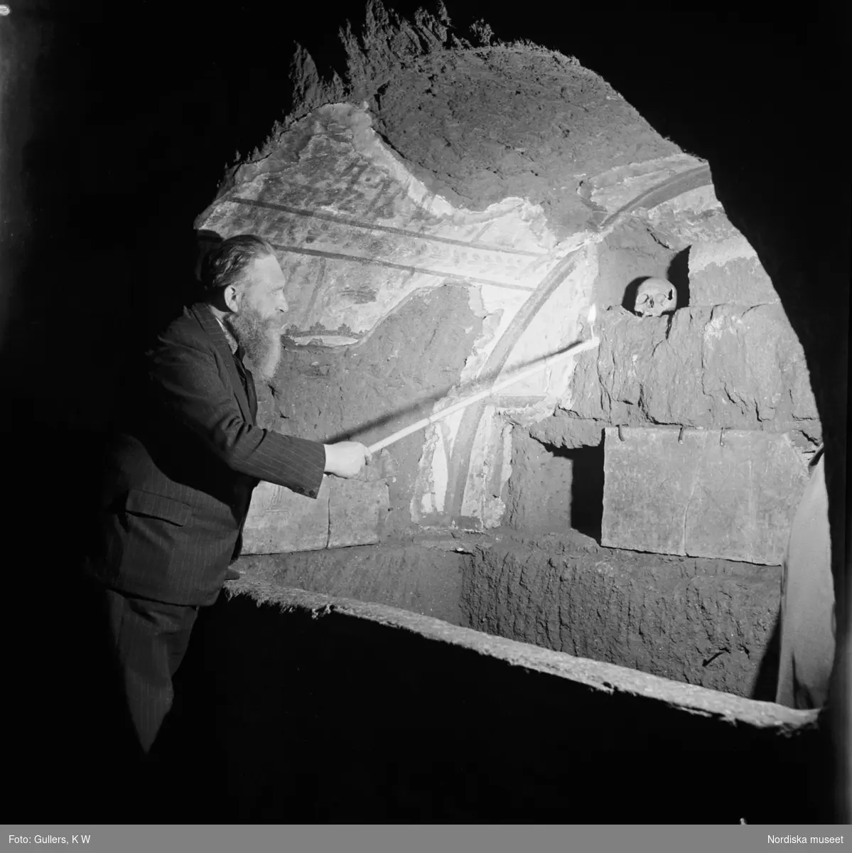 En man med pekpinne pekar ut en dödskalle i en av Roms katakomber
