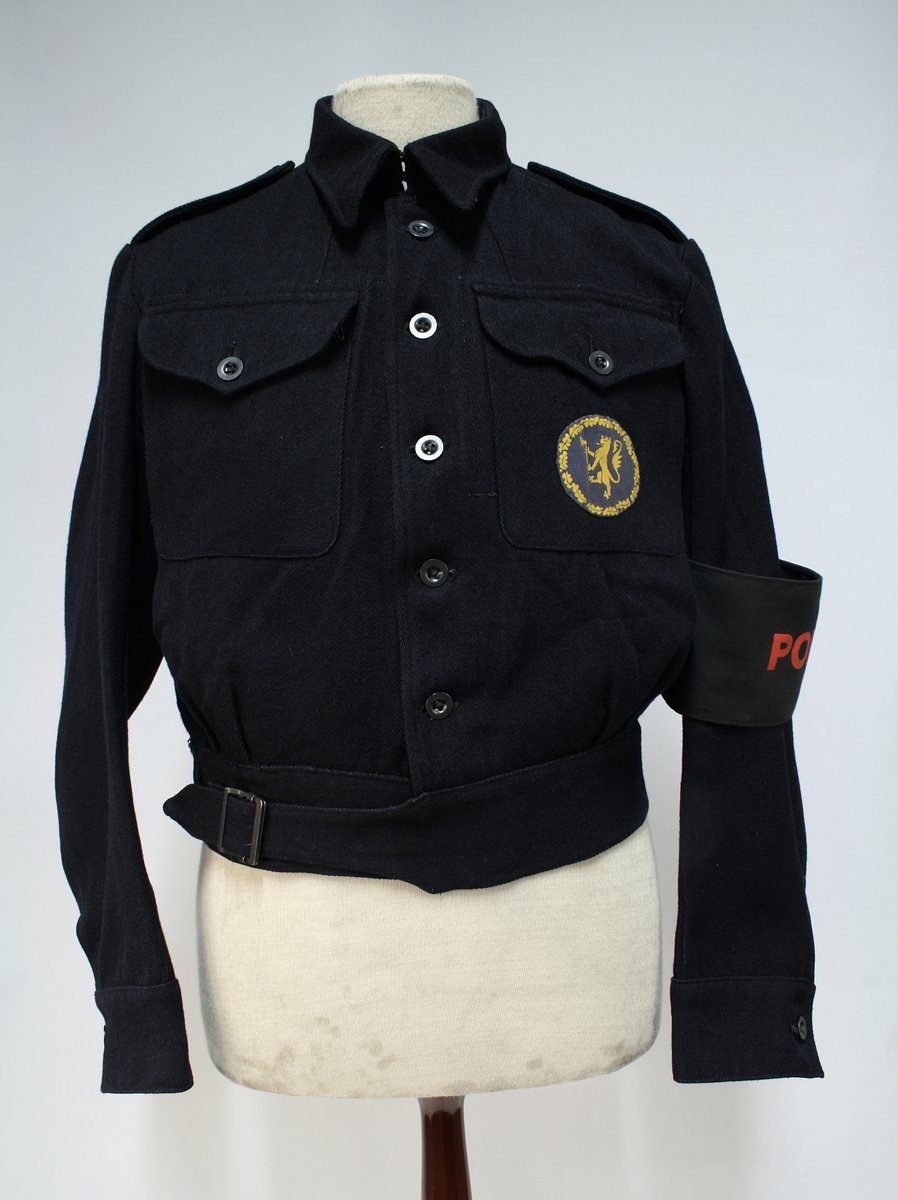 Mørkeblå battledress og lue av typen benyttet av de britiske ARP services. 

Enkeltkneppet jakke med innstramming i linningen, stoffmerke sydd på brystet, og politiarmbind. Beret med det engelskproduserte luemerket.