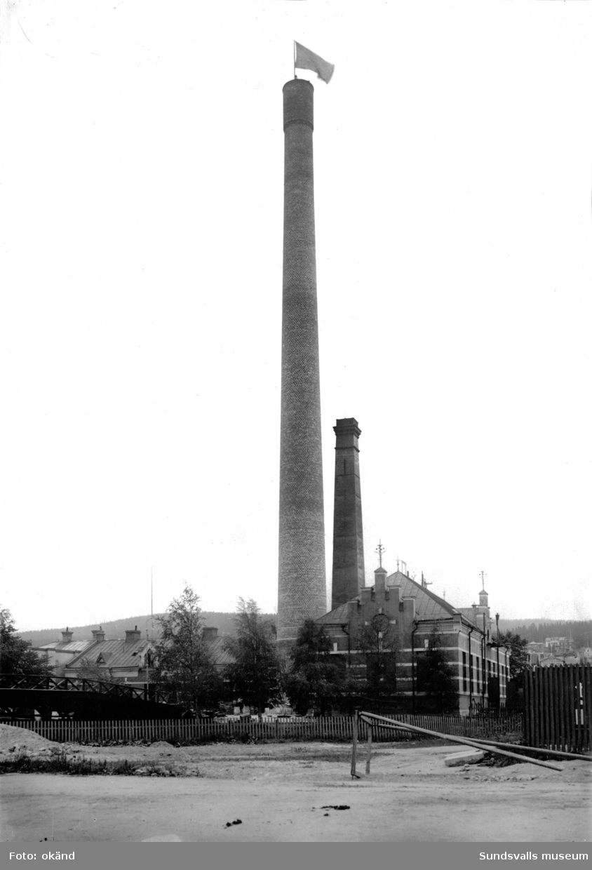 Elverket och gasverket sett mot sydost. Bakom den höga gasverksskorstenen står den ursprungliga mindre skorstenen (byggd 1866-1867) kvar. Den smala gångbron över järnvägen, med träräcken, ses till vänster. Den 57 m höga skorstenen revs i maj 1951.