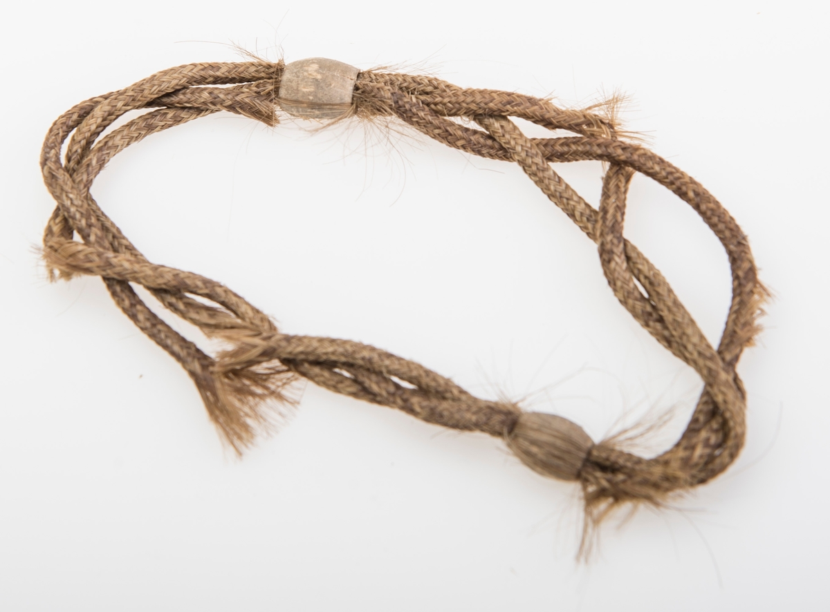 Armbånd laget av brunt hår med to treperler. Armbåndet består av tre flettede "rør" som er løst tvunnet sammen.