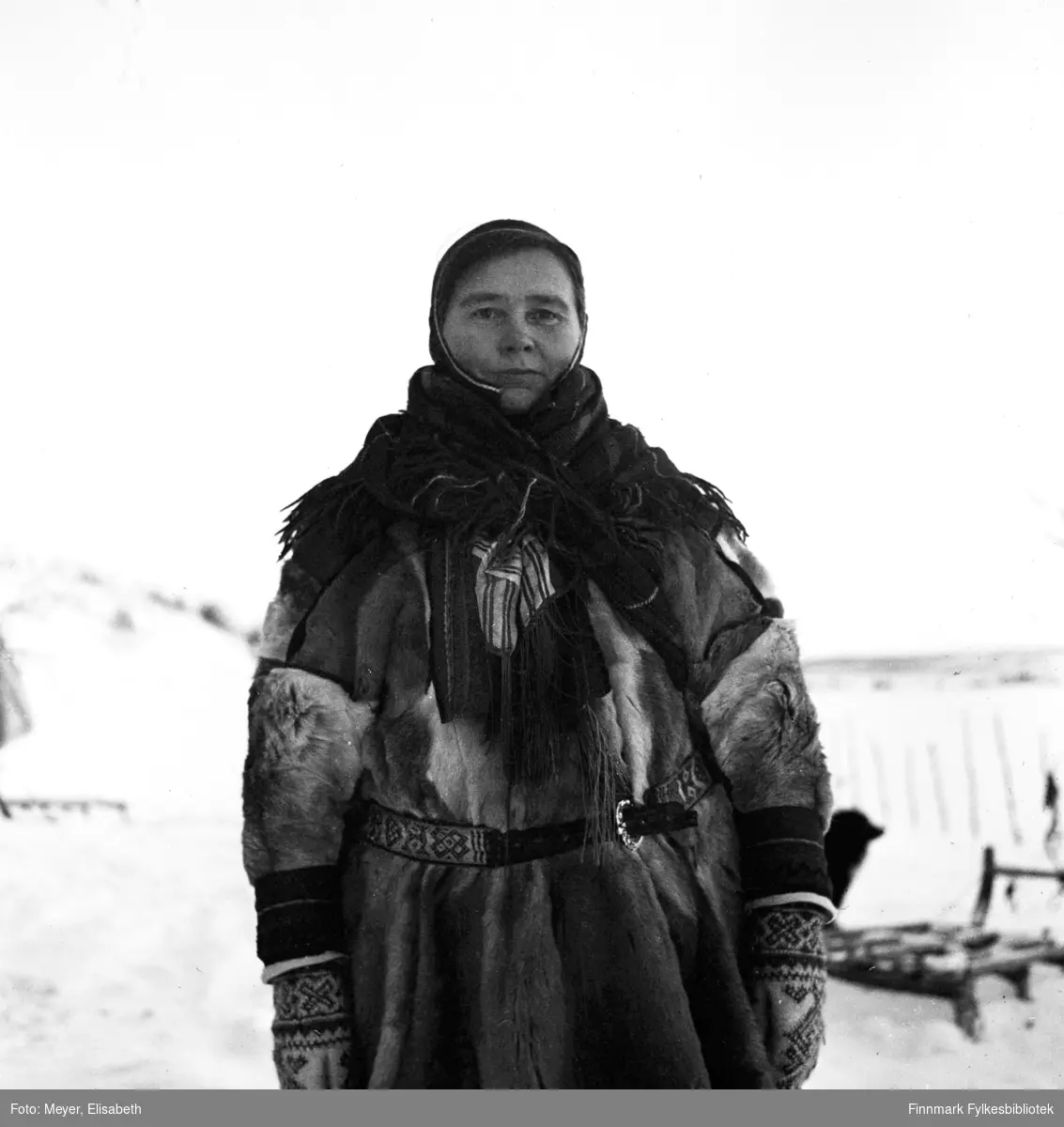 Ellen Johnsdatter Utsi kledd i samisk pesk med samisk belte, lue, sjal og votter. Fotografert av Elisabeth Meyer, mulighens i perioden rundt påske 1940.