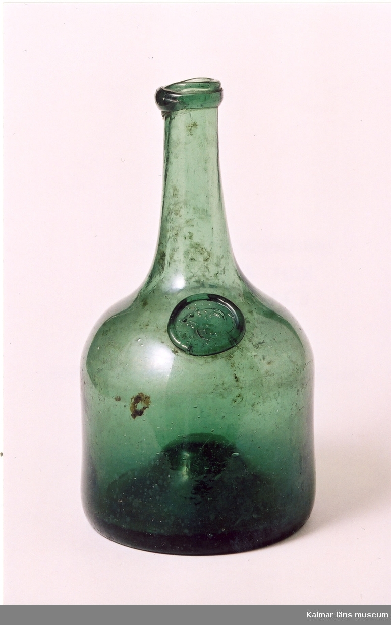 KLM 24961 Flaska, av grönt glas. Balongflaska. Hög kulle i botten. På skuldran ett glassigill. På sigillet stämpel: 1/3, L W G B. (LångWiks GlasBruk). Datering, omkring 1800-1815(?).