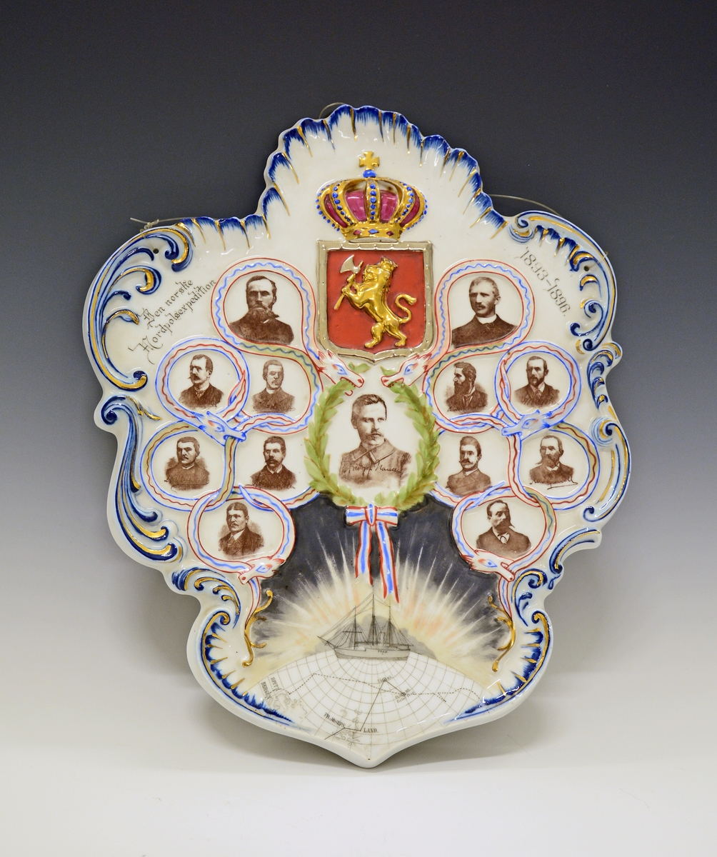 Fra protokollen: 
Porselensplatte:  "Den norske Nordpols-expedition 1893-1896", laget på Porsgrunds Porselænsfabrik. Platten har hvit bunn og er formet som et løvblad, kantet i blått og gull. Øverst det norske riksvåpen, ellers bilder av alle polfarerne, med Fritjof Nansen i midten. Rundt dette bildet laurbærkrans i grønt med sløyfe i de norske farger. I alt 13 personer. Nederst en del av en globus med tegning av polarskuta "Fram" på Nordpolen.