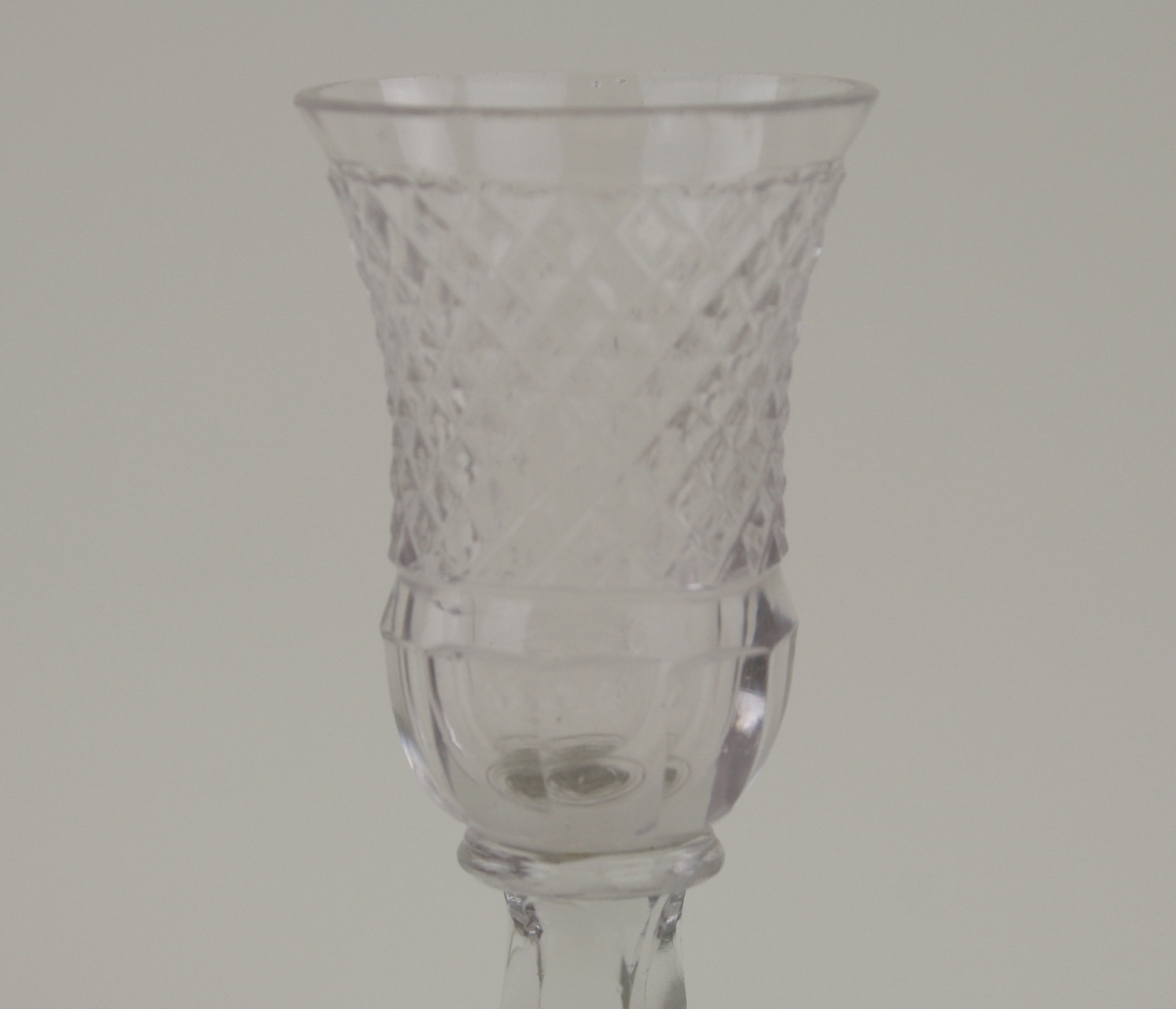 Glas av vitt glas med en fyrkantig fot. Kuppan har en slipad dekor med ett rutmönster och därunder slipade ovaler.