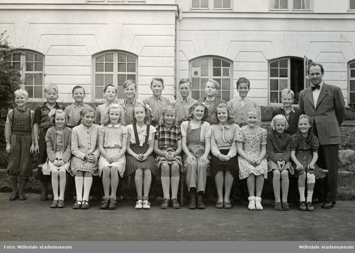 Elever (5:e klass) och magister Per Hasselgren står uppställda utanför Krokslättsskolan år 1949. Ninnie Johansson (gift Martin) sitter längst till vänster med uppsatt hår och stor rosett. Hennes familj bodde i ett flerfamiljshus som låg mittemot skolgården.