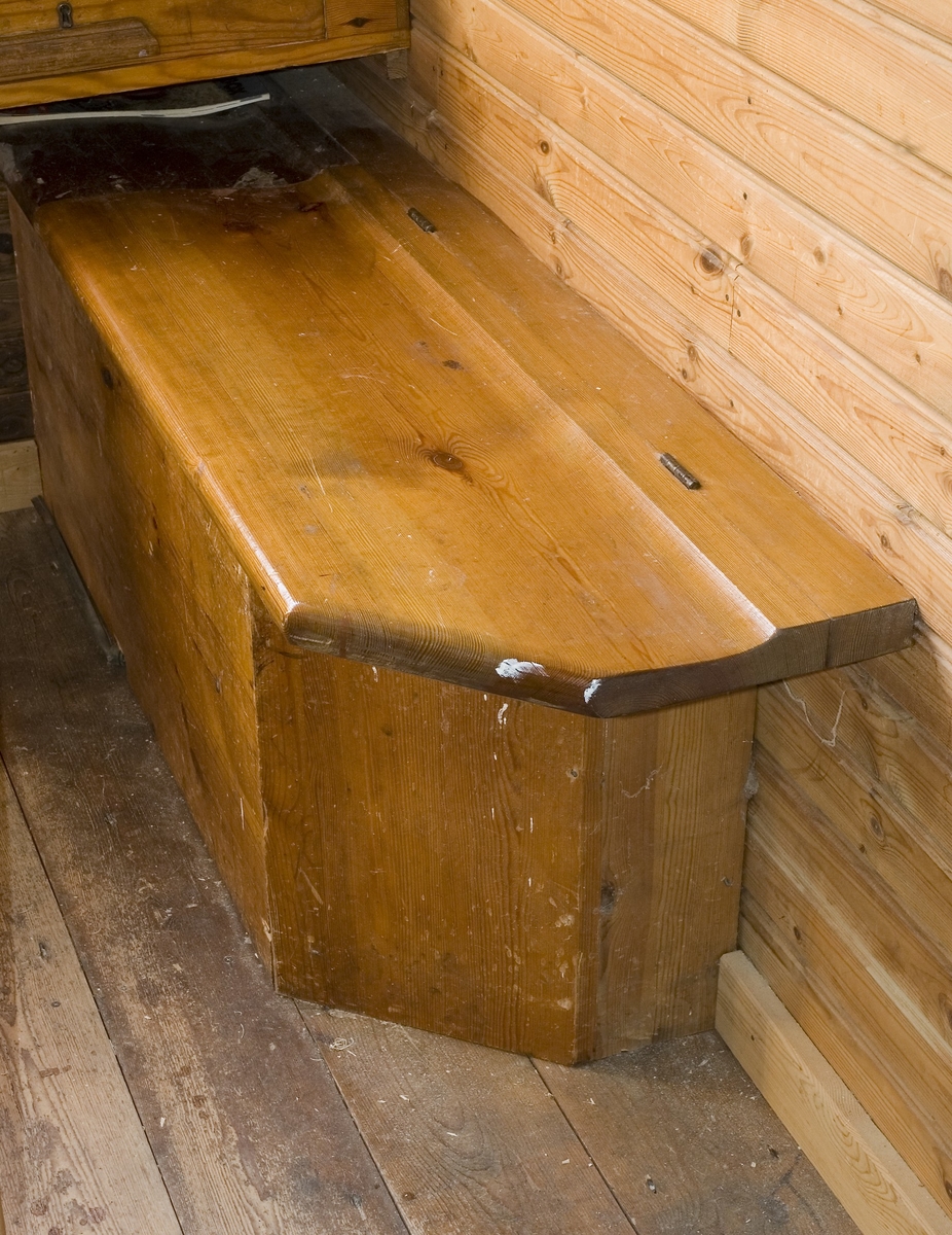 Väggbänk av trä med uppfällbar sittbräda. Under locket finns förvaringsutrymme i den låda som skapats av den väggfasta sittbänken. Väggbänkens ena ytterhörna har ett vinklat hörn. Väggbänken har tidigare funnits i kontoret på Dahlgrens Snickeri i Nacka och har flyttats över till snickerifabriken vid återuppbyggnaden år 1987. Bänken är klarlackad.

Funktion: Möbel att sitta på, förvara i