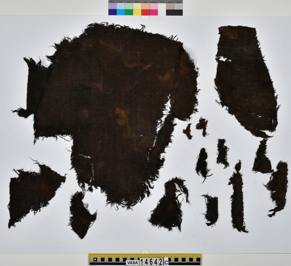 Textil.
132 fragment uppdelade på fyndnummer 14642a-f.
Fnr 14642a består av 42 fragment av ull vävda i tuskaft. Tyget har varit valkat på ena sidan. Många av fragmenten har bevarade originalkanter med sömmar och fållar.
Fnr 14642b består av 2 fragment av ull vävt i 2/1-kypert. Fragmentet har en bevarad originalkant.
Fnr 14642c består av 14 fragment av ull vävda i 2/2-kypert. Flera av fragmenten har en bevarad originalkant.
Fnr 14642d består av 28 fragment av ull vävda i 2/1-kypert. Fyra av fragmenten har en bevarad originalkant. Flera av fragmenten består bara av lösa trådar.
Fnr 14642e består av 9 fragment (4 större samt 5 mycket små) av ull vävda i tuskaft. Tyget har varit valkat på ena sidan. Fragmenten har bevarade originalkanter med spår av sömmar.
Fnr 14642f består av 37 fragment av ull vävda i tuskaft. Flera av fragmenten har bevarade originalkanter med fållar och spår av sömmar.