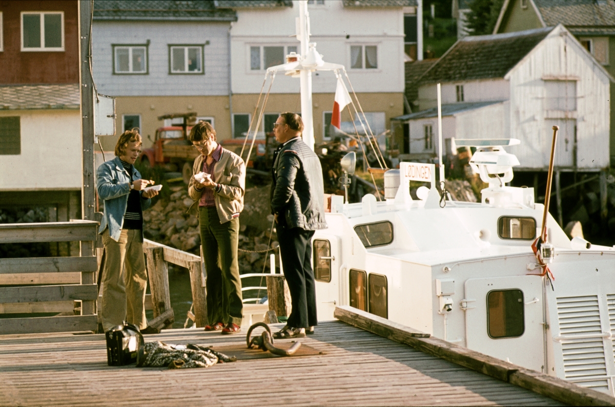 Tre menn på en kai. Til høyre ligger losbåten "Lødingen".